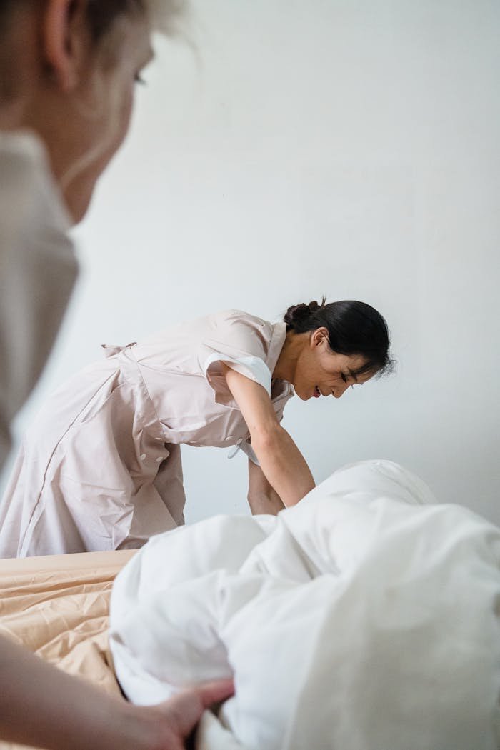gallery-4 Housekeeper diligently making a bed with pristine white linens in a hotel room.